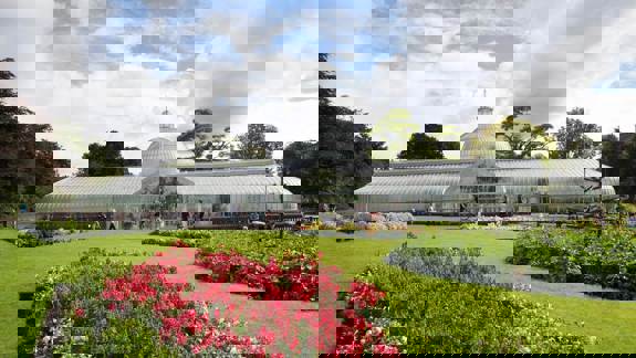 A wide shot of the Kibble Palace glasshouse in Glasgow's Botanic Gardens on a sunny day.