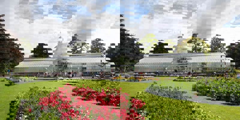 A wide shot of the Kibble Palace glasshouse in Glasgow's Botanic Gardens on a sunny day.
