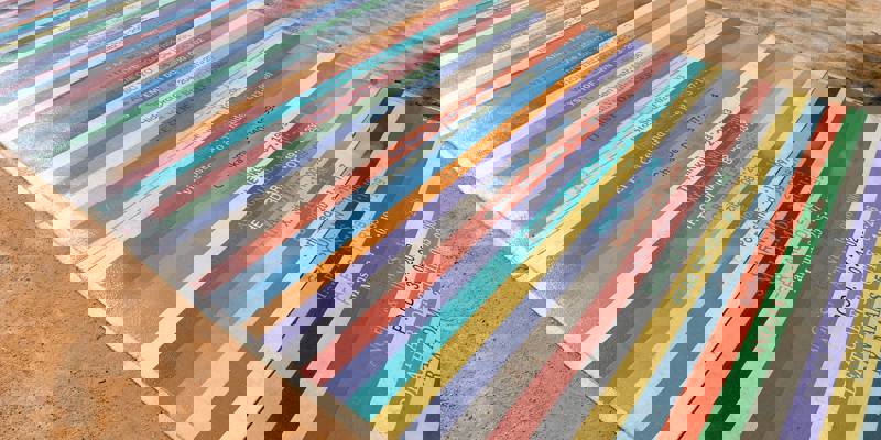 An outdoor path is decorated with colorful, striped panels featuring a list of artists and dates.