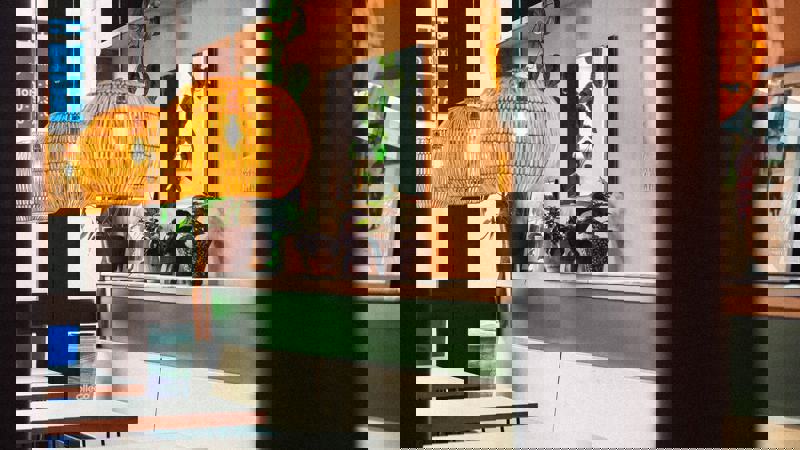 An interior view of a restaurant with a colorful design, hanging plants, and woven light fixtures.