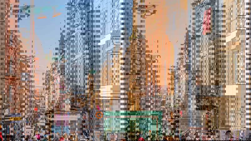 Buchanan Street, Glasgow, bustling with shoppers under a clear sky, featuring historical architecture, modern shopfronts like H&M, and a Subway entrance.