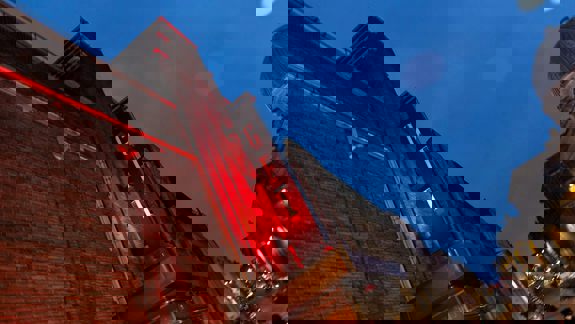 The brightly lit front of the Glasgow Film Theatre (GFT) building at dusk, with its red sign glowing. 