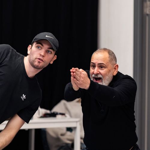 Two men are engaged in an enthusiastic discussion. The man on the left, in a black cap, leans forward, while the older man gestures expressively.