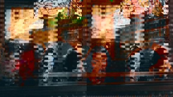 A group of people sitting at a booth-style table in a dimly lit bar with a stained-glass lampshade hanging above them.