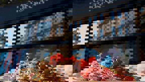 Close-up of a plate of French toast topped with strawberries, held in front of a cafe with a sign reading "Rose & Grants."