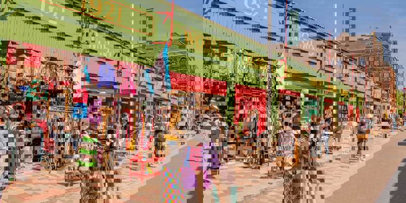 Outdoor market stalls with colorful clothing, mannequins, and people Browse under a blue sky.