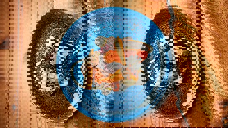 An overhead shot of a blue ceramic plate with a gourmet meal on a rustic wooden table.