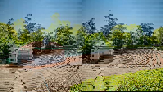 Tiered seating and stage at Kelvingrove Bandstand on a sunny day, with trees in the background.