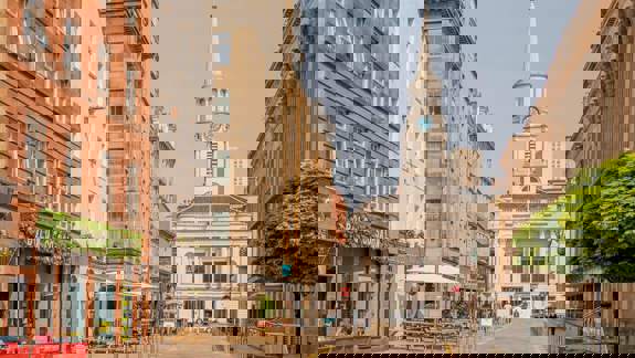 A wide street view showing historic architecture in Glasgow, including a church with a tall steeple and clock face, and several cafes