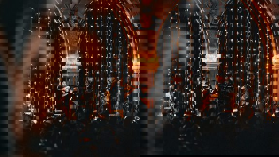 String quartet performing beneath fairy lights inside Òran Mór, with audience members watching in candlelit atmosphere.