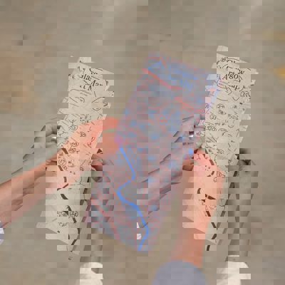 A pair of hands holds a folded map titled "Glasgow Art Map." The map features blue lines and pink-colored roads.