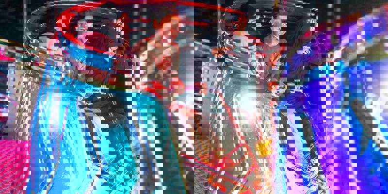 Four individuals are seated and laughing in a bright blue, spinning fairground ride compartment at the Irn Bru Carnival.