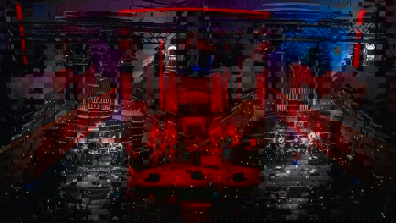 An audience watches a band play a concert in the Saint Luke's Glasgow music venue, featuring a balcony and disco ball.