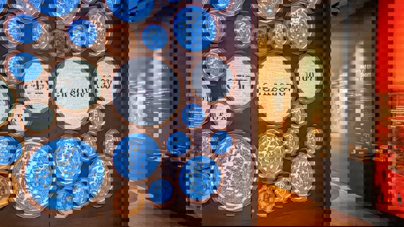 An interior shot of an exhibition with large circular art pieces on a wall, some with text like "CITY GLASGOW 1903".