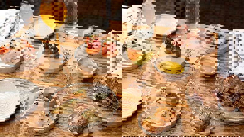 A wooden table laden with various plates of artfully presented food and drinks in an outdoor setting.