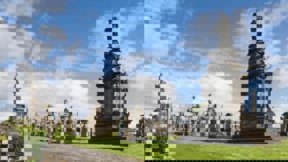 A bright, clear day shows a large cemetery on a grassy hill filled with elaborate stone monuments.
