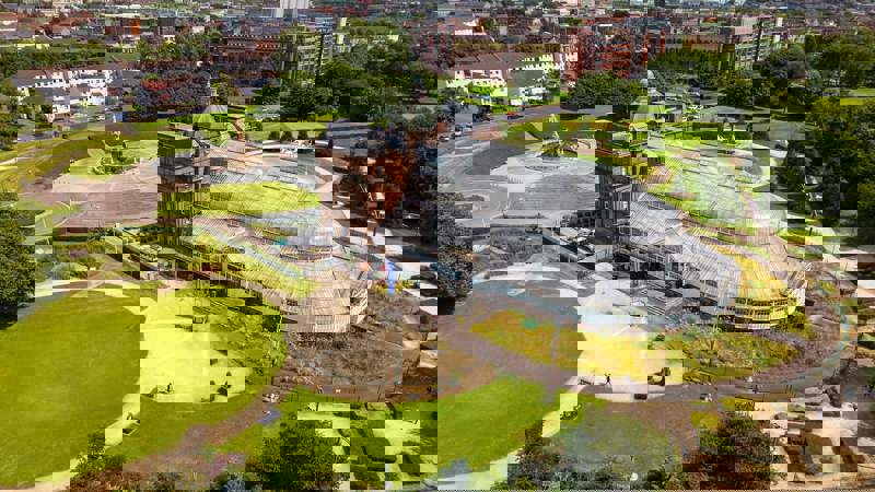 An aerial view of the People's Palace and Winter Gardens glasshouse in Glasgow Green, surrounded by green lawns.