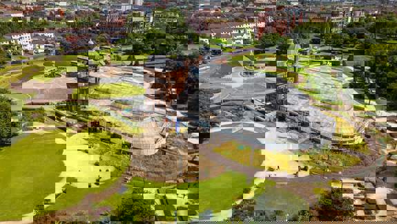 An aerial view of the People's Palace and Winter Gardens glasshouse in Glasgow Green, surrounded by green lawns.