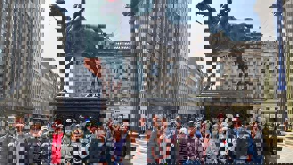 A group of people gathered in front of a statue with a traffic cone on its head.