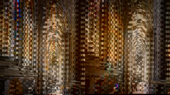 Inside Glasgow Cathedral, sunlight illuminates the ancient stone arches and vaulted ceilings. A large stained-glass window on the left side adds a splash of colour to the historic nave.