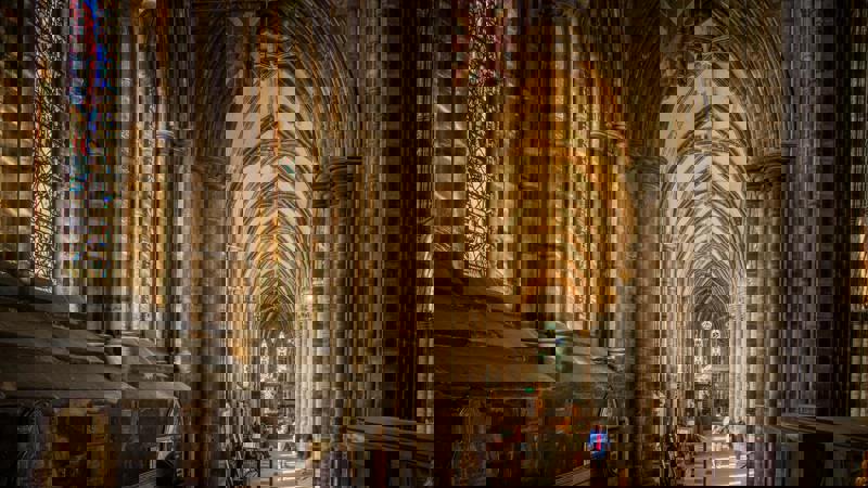 Inside Glasgow Cathedral, sunlight illuminates the ancient stone arches and vaulted ceilings. A large stained-glass window on the left side adds a splash of colour to the historic nave.