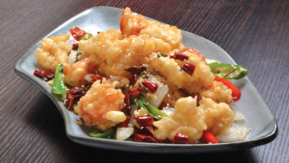 Plate of crispy fried shrimp garnished with peppers on a dark wooden table.
