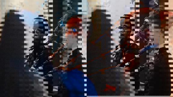 Two men playing bagpipes in the National Piping Centre, Glasgow, with one man in the foreground and the other looking on, surrounded by display cases.