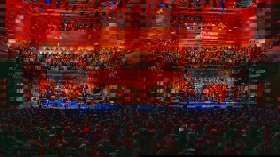 A performance hall with a large choir on risers and a group of musicians on stage, performing for a seated audience.