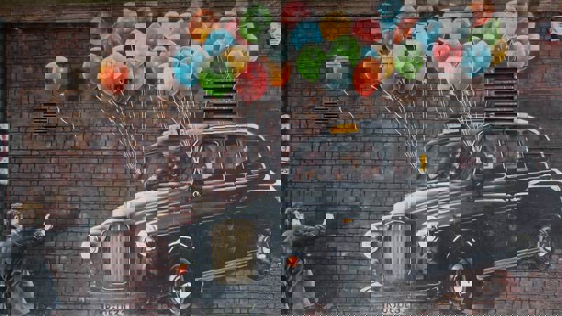 Mural of a black taxi cab floating with balloons, as a man reaches out to it.