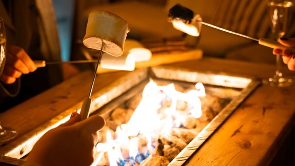 People toasting marshmallows over an outdoor firepit at night, creating a cosy autumn atmosphere.